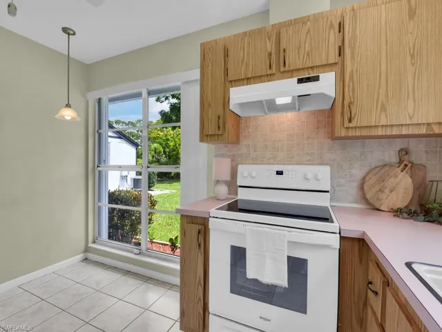 Kitchen with electric stove, under cabinet range hood, light countertops, tasteful backsplash, and decorative light fixtures