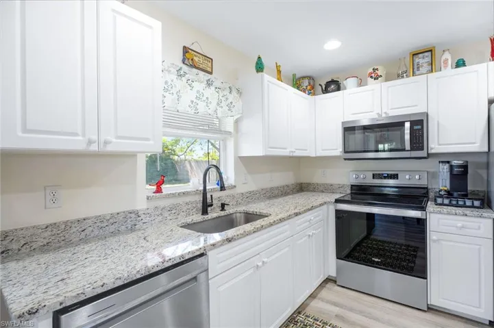 Kitchen with stainless steel appliances, light stone counters, sink, light wood-type flooring, and white cabinetry