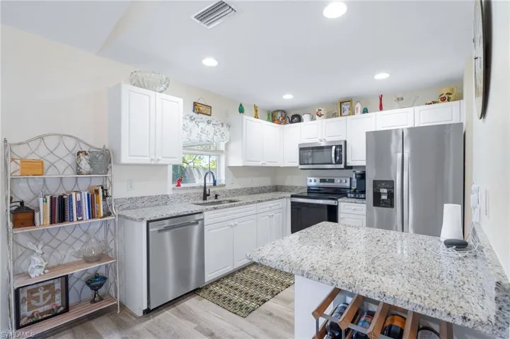 Kitchen featuring appliances with stainless steel finishes, a breakfast bar area, light stone countertops, sink, and white cabinetry