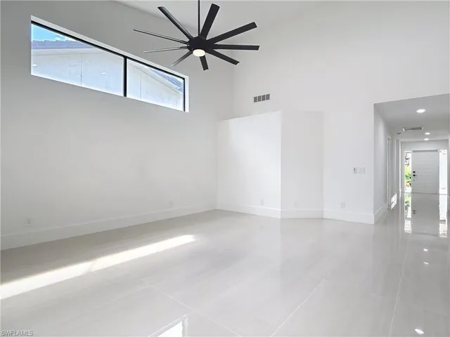 Empty room with light tile patterned floors, a ceiling fan, and a high ceiling