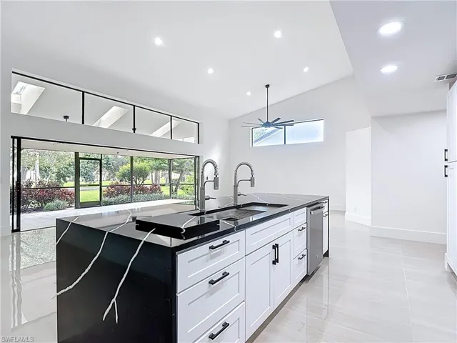 Kitchen with lofted ceiling, recessed lighting, a skylight, an island with sink, and white cabinets