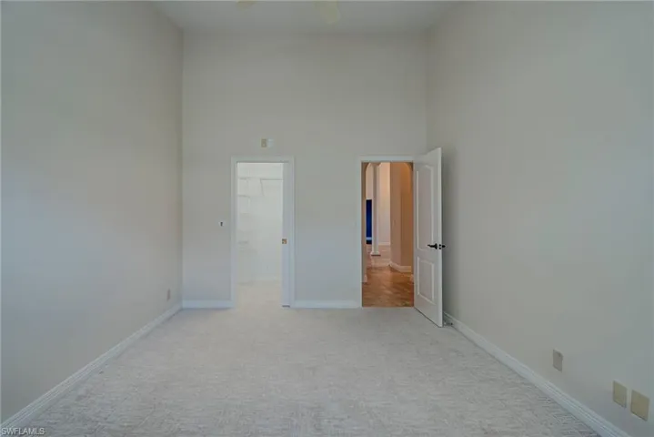 Unfurnished bedroom with a spacious closet, light carpet, a high ceiling, and a ceiling fan