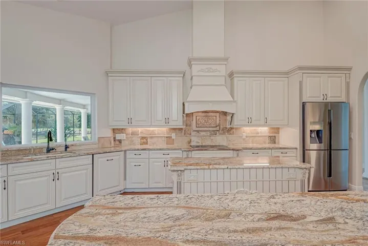 Kitchen featuring stainless steel fridge, light stone counters, white cabinets, decorative backsplash, and a high ceiling
