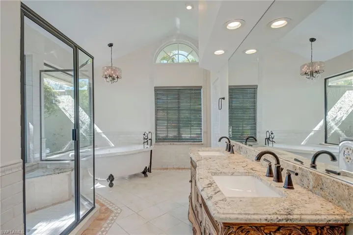 Bathroom with hanging lights, a soaking tub, double vanity, light tile patterned floors, and tile walls