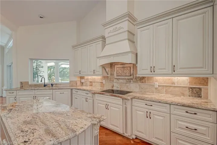 Kitchen featuring light cherry wood floorslight stone counters, tasteful backsplash, black electric stovetop, and cream cabinets