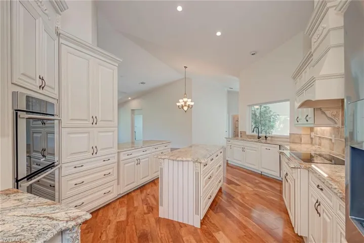 Kitchen with a peninsula, stainless steel appliances, cherry wood floors, light stone countertops, and vaulted ceiling