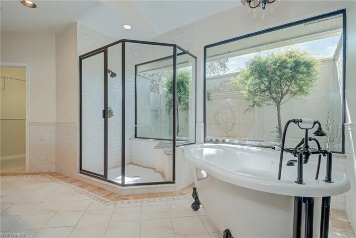 Full bathroom featuring a shower stall, a freestanding bath, a walk in closet, light tile patterned floors, and tile walls