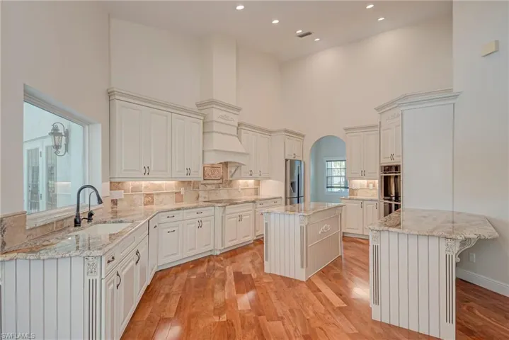 Kitchen featuring a center island, a peninsula, cherry wood flooring, light stone counters, and arched walkways