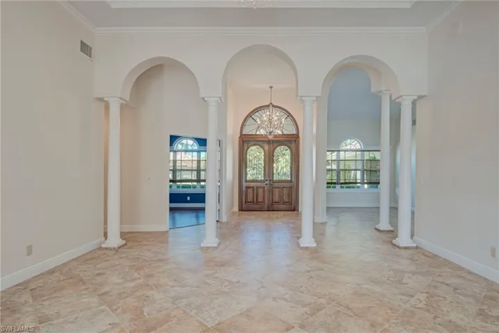 Foyer entrance featuring hanging lights, a high ceiling, ornate columns, crown molding, and arched walkways