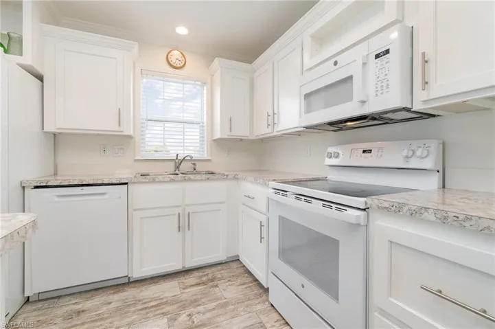 Kitchen with crown molding, primwhite appliances, decorative light fixtures, a center island, and a kitchen breakfast bar