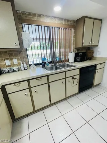 Kitchen featuring light countertops, backsplash, black dishwasher, and light tile patterned floors