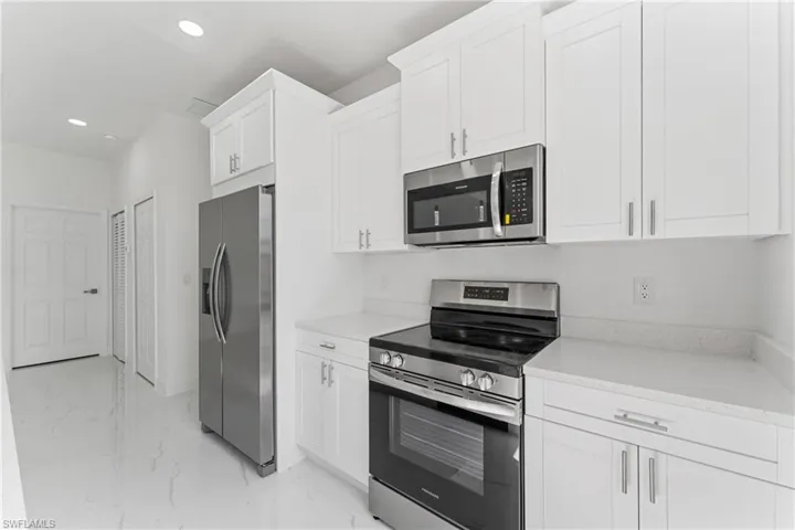 Kitchen with light stone counters, marble finish floor, recessed lighting, appliances with stainless steel finishes, and white cabinets