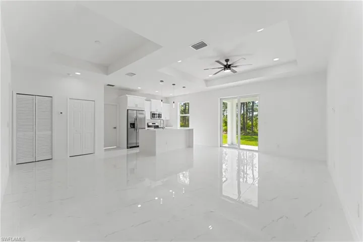 Unfurnished living room featuring marble finish floor, a raised ceiling, visible vents, ceiling fan, and baseboards