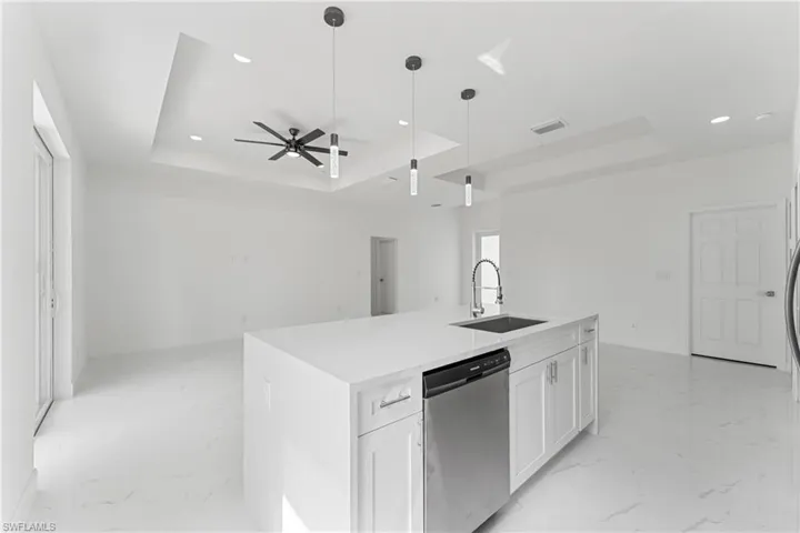 Kitchen with a sink, marble finish floor, a tray ceiling, and dishwasher