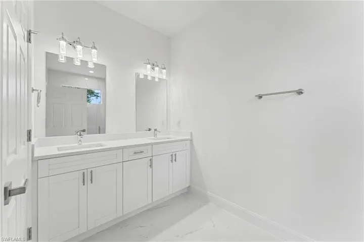 Full bathroom with double vanity, marble finish floor, baseboards, and a sink