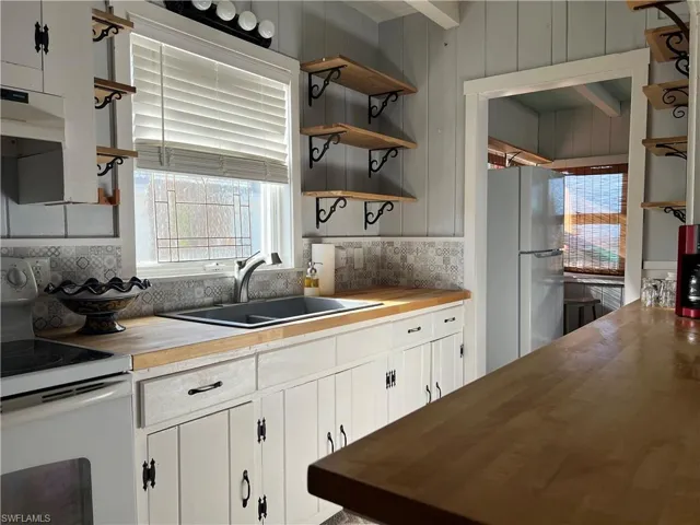 Kitchen with sink, butcher block counters, white cabinetry, and white appliances
