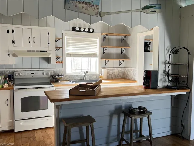 Current  Kitchen with wooden counters, white range with electric stovetop, white cabinetry, and a breakfast bar
