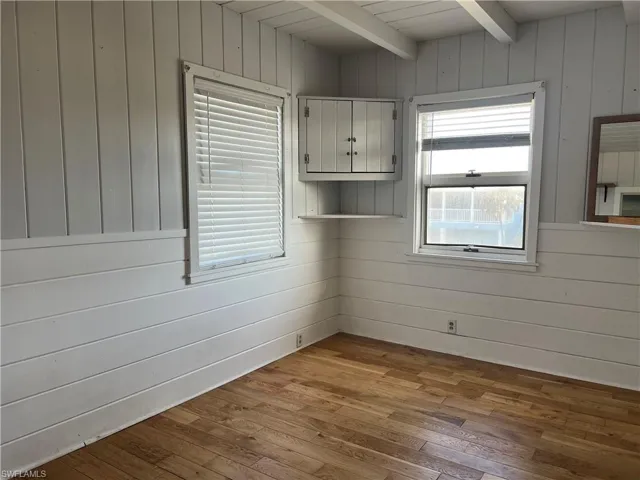 Current  view primary bedroom  featuring plenty of natural light, beam ceiling, wood walls, and light wood-type flooring