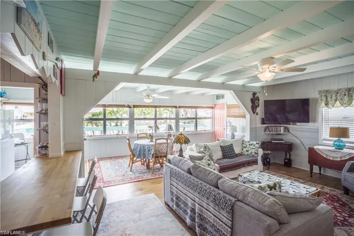 Living room prior to Hurricane Helene featuring beam ceiling, wooden walls, light hardwood / wood-style flooring, and ceiling fan