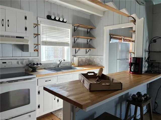 Current  Kitchen with white cabinets, stainless steel refrigerator, electric stove, wooden counters, and sink