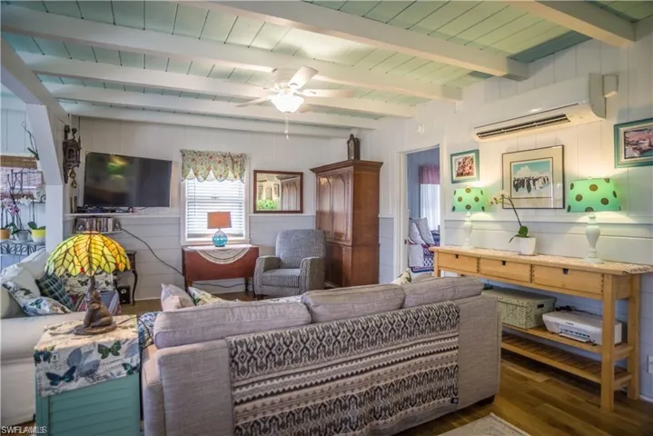 Living room with ceiling fan, a wall mounted air conditioner, vaulted ceiling with beams, wood walls, and dark wood-type flooring