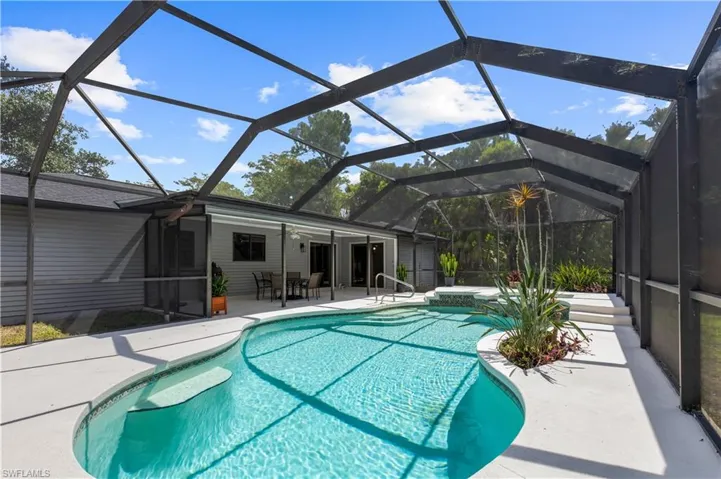 Outdoor pool featuring an in-ground hot tub, a patio area, and glass enclosure
