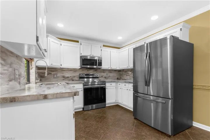 Kitchen featuring appliances with stainless steel finishes, backsplash, light countertops, white cabinetry, and ornamental molding