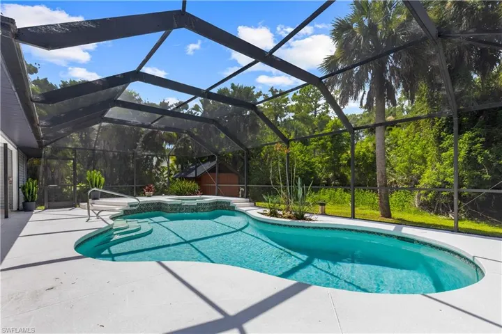 View of pool featuring a patio area, a storage unit, a pool with connected hot tub, and glass enclosure