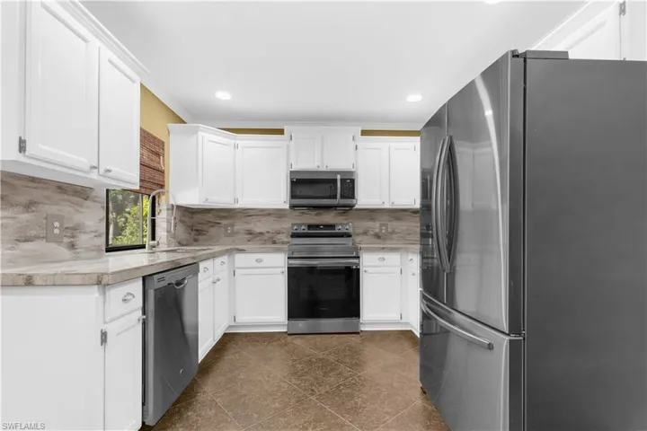Kitchen with stainless steel appliances, tasteful backsplash, light countertops, white cabinetry, and crown molding