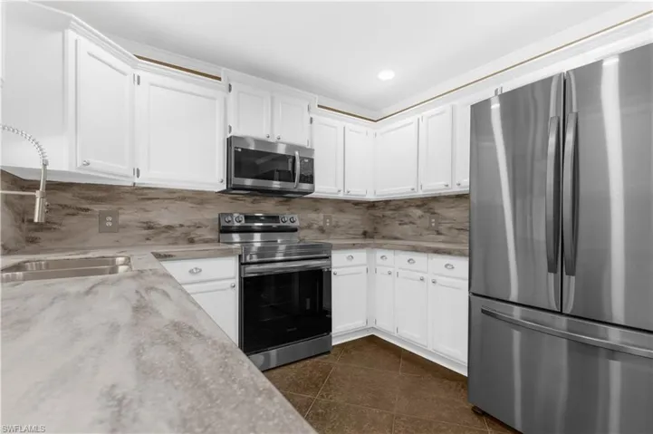 Kitchen with appliances with stainless steel finishes, white cabinetry, dark tile patterned flooring, decorative backsplash, and light stone countertops