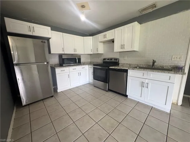 Kitchen with stainless steel appliances, light tile patterned floors, white cabinetry, and light stone counters