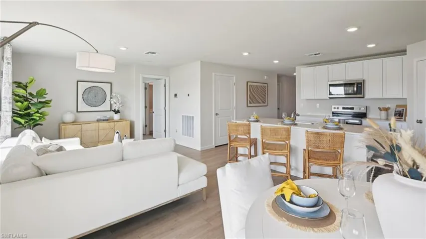 Model Home. The property features an open-concept living area with light-colored flooring, a kitchen with white cabinetry and stainless steel appliances, and a breakfast bar with seating