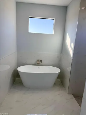 Bathroom with a wainscoted wall, a soaking tub, light marble finish floors, and tile walls