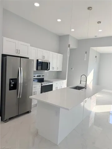 Kitchen with appliances with stainless steel finishes, pendant lighting, white cabinets, light stone countertops, and recessed lighting