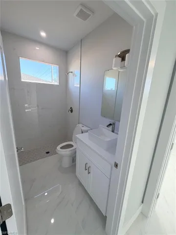 Bathroom with vanity, a marble finish shower, and light marble finish floors