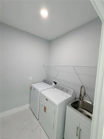 Laundry area featuring light marble finish floors and washer and clothes dryer