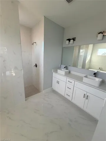 Bathroom with a marble finish shower, double vanity, and light marble finish flooring