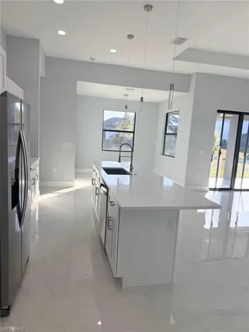 Kitchen with light stone counters, appliances with stainless steel finishes, recessed lighting, a kitchen island with sink, and white cabinets