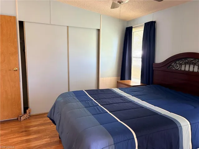 Bedroom with a textured ceiling, wood finished floors, a ceiling fan, a decorative wall, and a closet