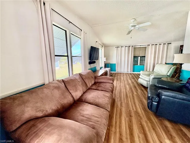 Living room with lofted ceiling, wood finished floors, a textured ceiling, and ceiling fan