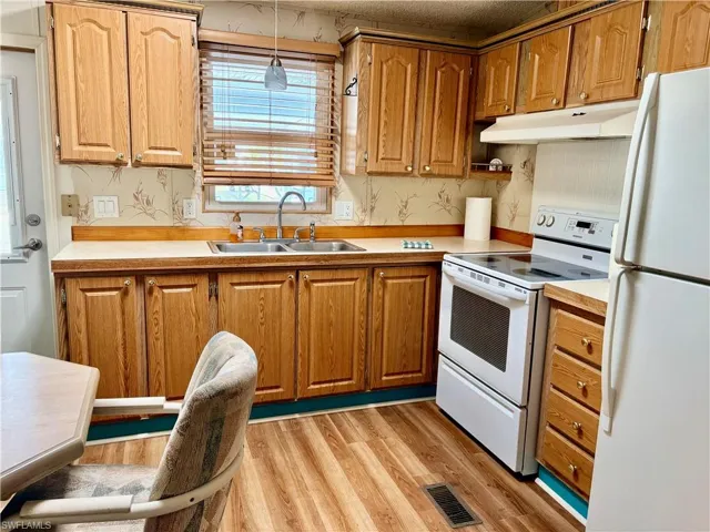 Kitchen with white appliances, light countertops, light wood-style flooring, under cabinet range hood, and brown cabinetry