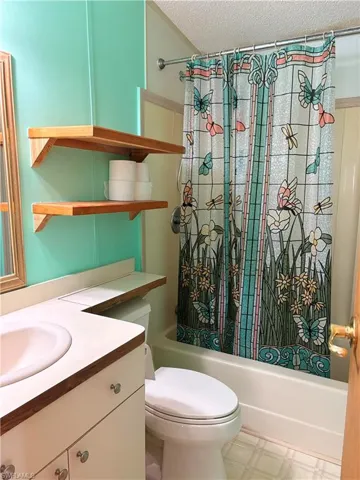 Bathroom featuring shower / bath combination with curtain, light floors, a textured ceiling, and vanity