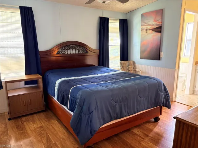 Bedroom featuring wainscoting, wood finished floors, ceiling fan, a textured ceiling, and ensuite bathroom