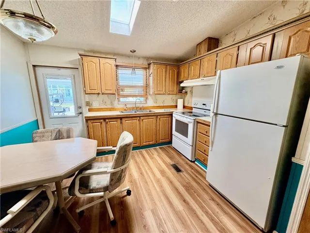 Kitchen featuring white appliances, a skylight, hanging light fixtures, light countertops, and a textured ceiling