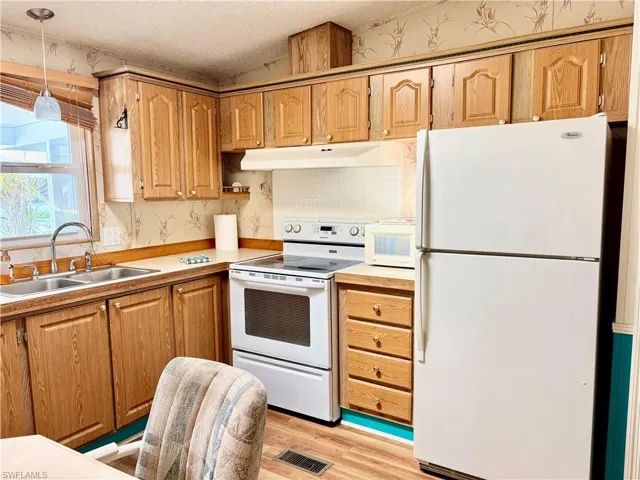 Kitchen featuring white appliances, lofted ceiling, light wood-style floors, light countertops, and under cabinet range hood