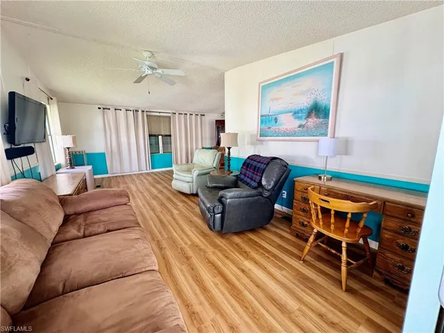 Living area featuring a textured ceiling, light wood finished floors, and ceiling fan