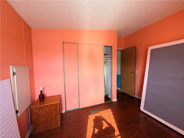 Unfurnished bedroom with a textured ceiling, dark wood-style floors, and a closet