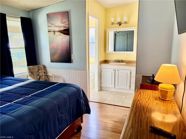 Bedroom with light wood-style floors, a wainscoted wall, a textured ceiling, and ensuite bathroom