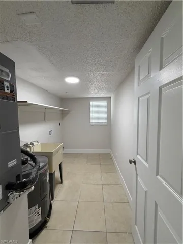 Laundry room with hookup for a washing machine, water heater, a textured ceiling, heating unit, and light tile patterned flooring