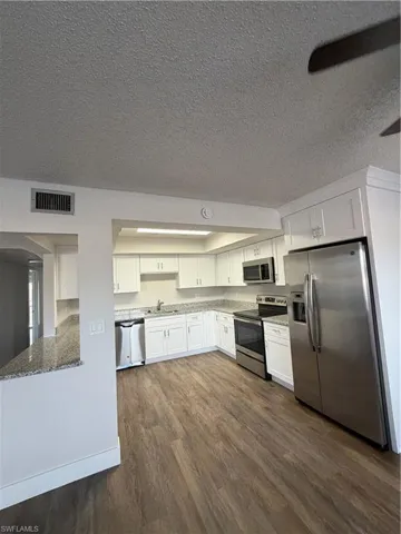 Kitchen with fridge, white cabinetry, stainless steel stove, a textured ceiling, and dark wood-style floors